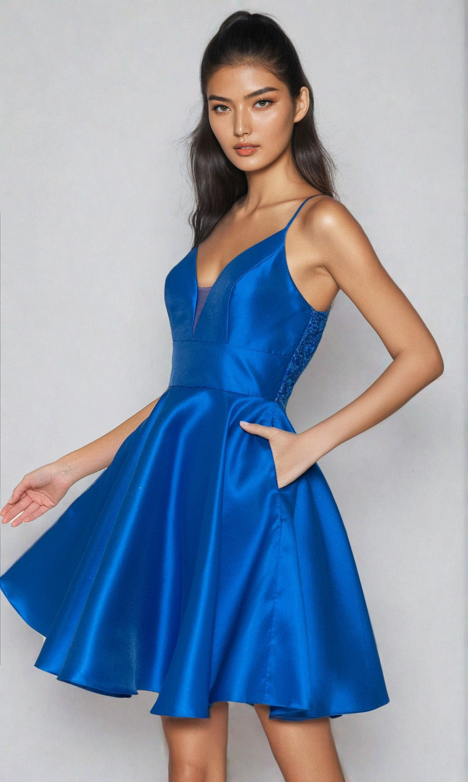 A woman poses against a plain light background wearing the Lace-Back Short A-Line Homecoming Dress 8698, a sleeveless satin party dress in deep blue with a flared skirt and pockets.